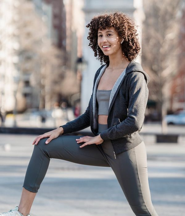 Woman in activewear smiling and stretching in a bright, modern room.